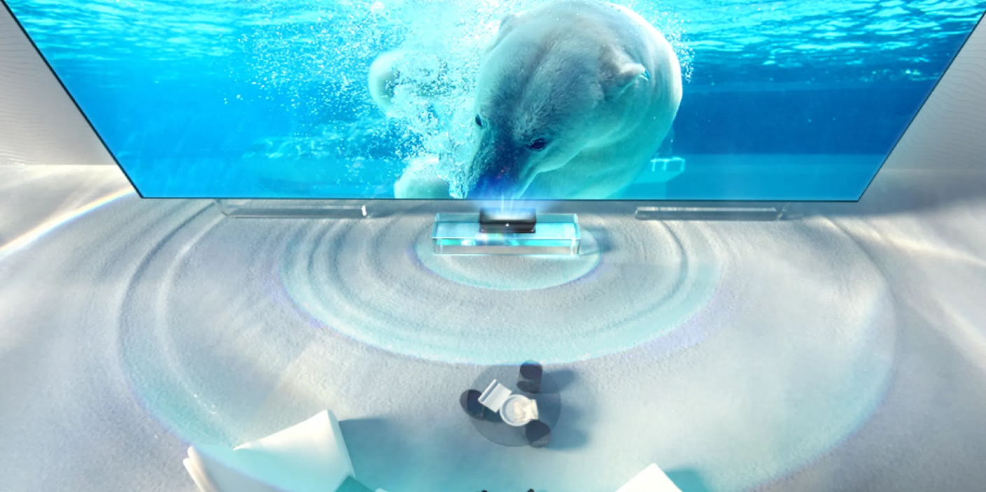 A wide-angle, aerial photograph showing an ultra-short-throw projector casting an image of a polar bear swimming in water onto a large screen placed on the floor in a minimalist, white room.